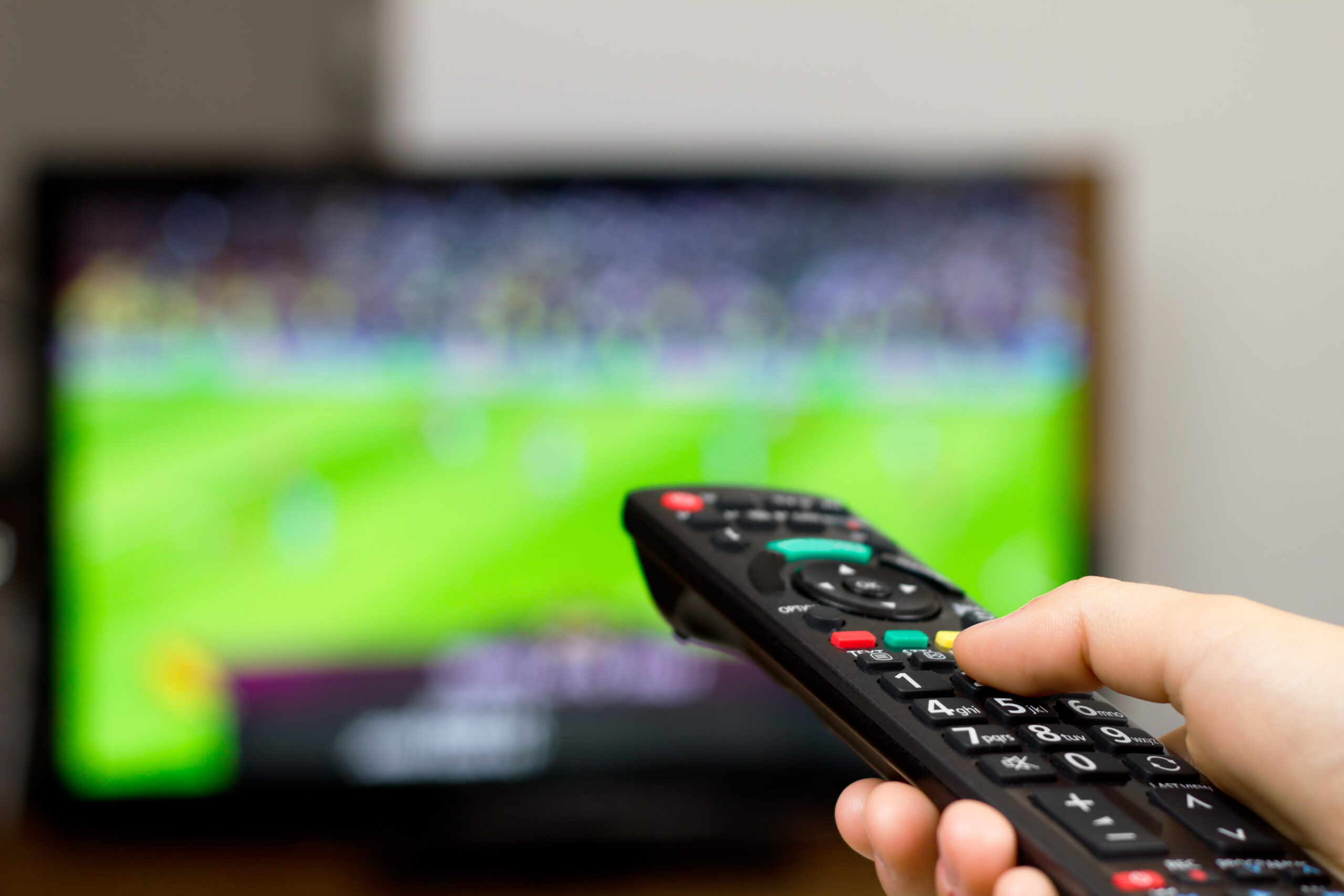 Person with remote control watching football on TV